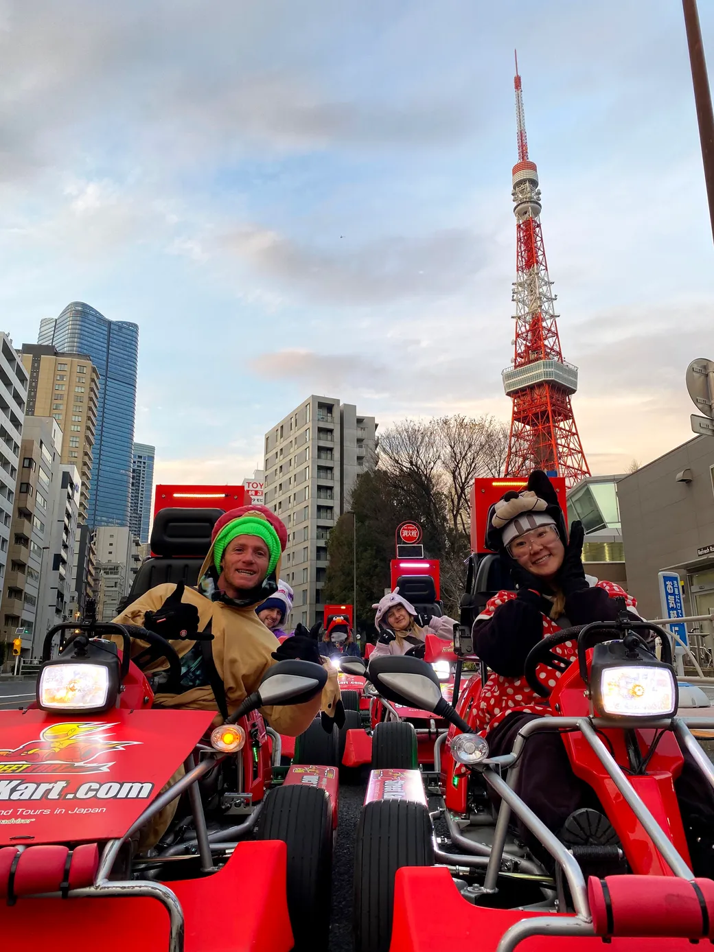 Group of people in red go-karts posing and smiling on a city street with Tokyo Tower in the background.